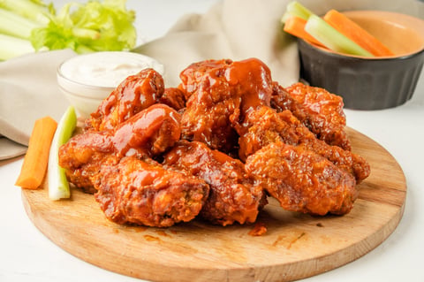 Fried BBQ wings served on wooden board with celery and blue cheese sauce