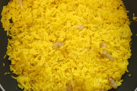 Fluffy yellow rice mixed with spices and herbs, simmering gently in a pot.