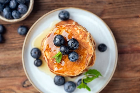 Stack of golden pancakes topped with blueberries and sweet maple syrup, top view, selective focus