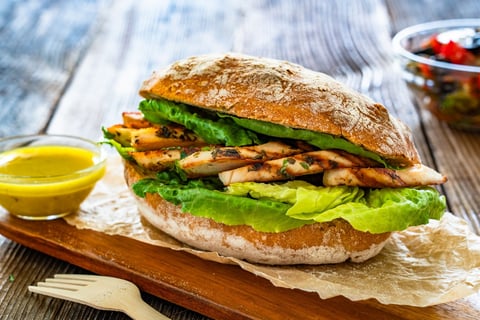 Takeaway sandwich with slices of grilled chicken breast on wooden table