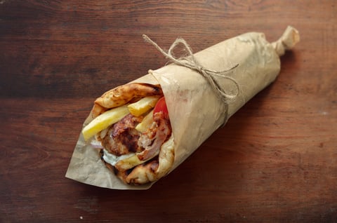 Traditional Greek gyros wrap with grilled meat, fries, and vegetables in pita bread on rustic wooden table