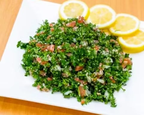 Tabbouleh salad on a white plate with fresh lemon slices garnish on a wooden table
