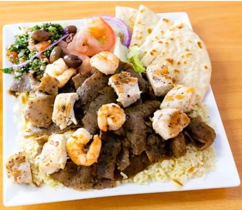 Mixed grilled seafood platter with shrimp, scallops, and fish over rice on a white plate with garnish