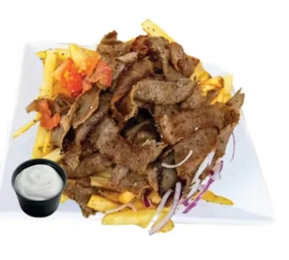 Plate of sliced grilled meat with french fries, red peppers, purple onions, and a side of white sauce dip