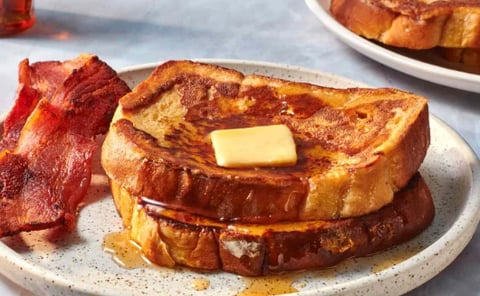 Golden French toast with butter on white plate, served with crispy bacon strips