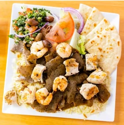 Mixed platter with grilled meats, shrimp, fresh salad, tomato slices, red onion, pita bread, and hummus on a white plate
