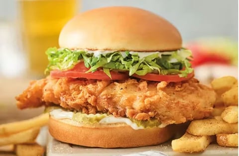 Crispy fried chicken sandwich with lettuce and tomato on a bun, served with french fries and a beverage