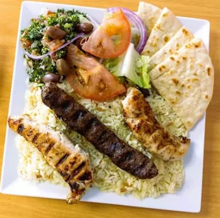 Grilled kebab platter with marinated meat skewers, rice, pita bread, fresh vegetables and tabbouleh salad on white plate