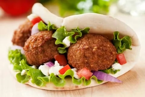 Two crispy falafel patties in a white pita pocket with fresh lettuce, tomatoes, onions, and white sauce on a wooden surface