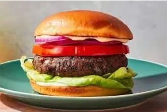 A beef burger with tomato, lettuce, and red onion on a toasted bun, served on a teal plate