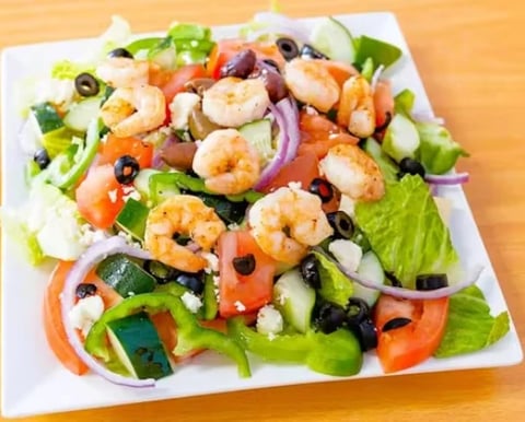 Fresh shrimp salad with mixed greens, black olives, red peppers, and purple onions on a white square plate