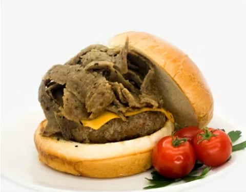 A messy burger with a thick meat patty, melted cheese, and caramelized onions on a bun, served with fresh tomatoes and parsley.
