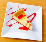 Slice of cheesecake with caramel topping and red sauce drizzle on a white square plate
