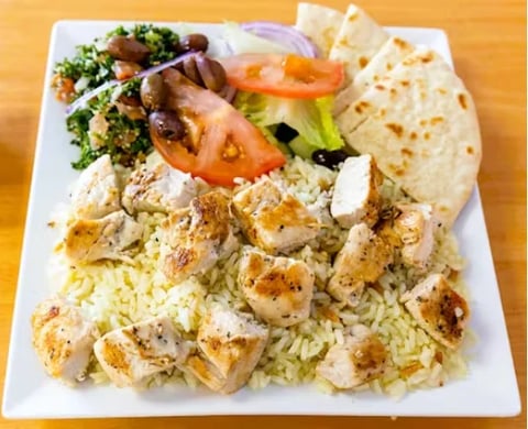 Grilled shrimp served over rice with fresh vegetables and matzah on a white plate