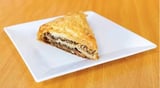 Slice of spinach and feta phyllo pie on a white square plate with wooden surface background