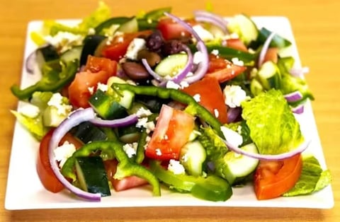 Colorful Greek salad on white plate with mixed greens, tomatoes, cucumbers, red onions, and crumbled feta cheese