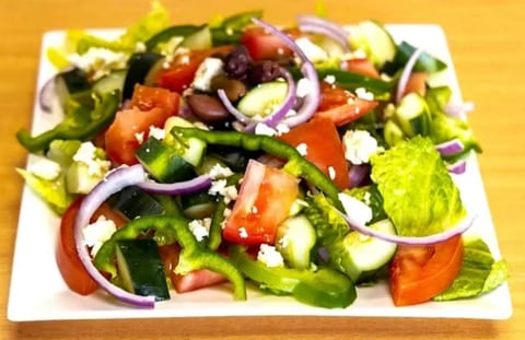 Fresh garden salad with mixed greens, tomatoes, cucumbers, red onions, and crumbled feta cheese on a white plate